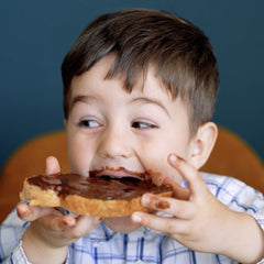 Copil care mușcă dintr-o felie de pâine cu cremă de alune Alunette cu cacao